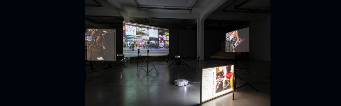 In einem dunklen Raum werden mehrere Videos auf Leinwänden und Bildschirmen abgespielt.