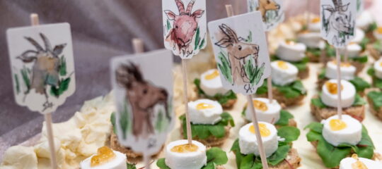 Detailaufnahme eines Banketts von Sonja Alhäuser mit kleinen Speisen und gezeichneten Tiermotiven auf Holzspießen.